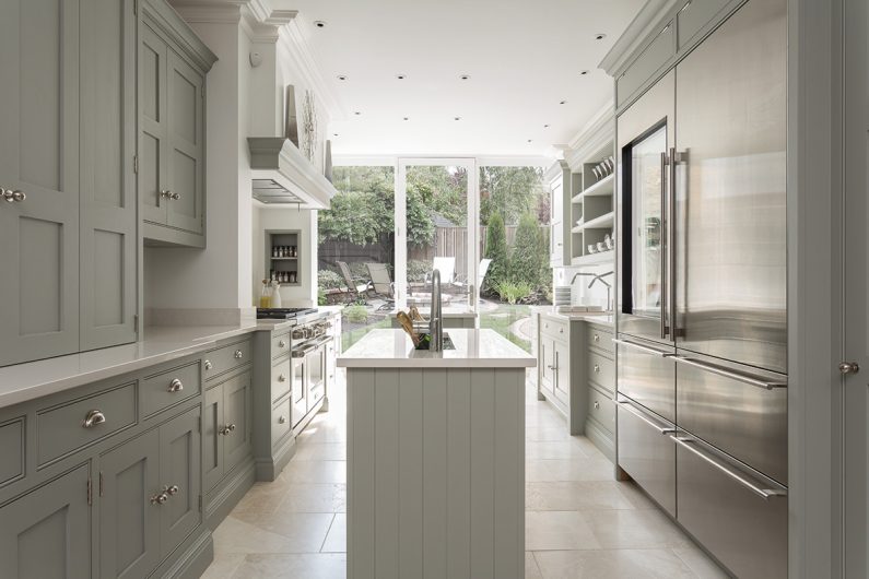 a narrow shaker kitchen in sage green with silver handles, a kitchen island and a large American-style fridge-freezer