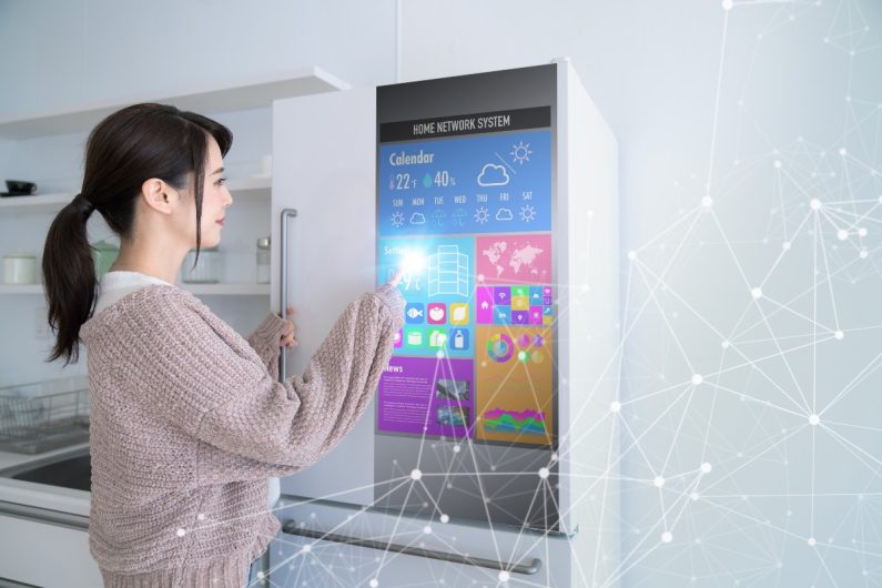 a woman in a light pink jumper touching the screen of an illuminated smart appliance